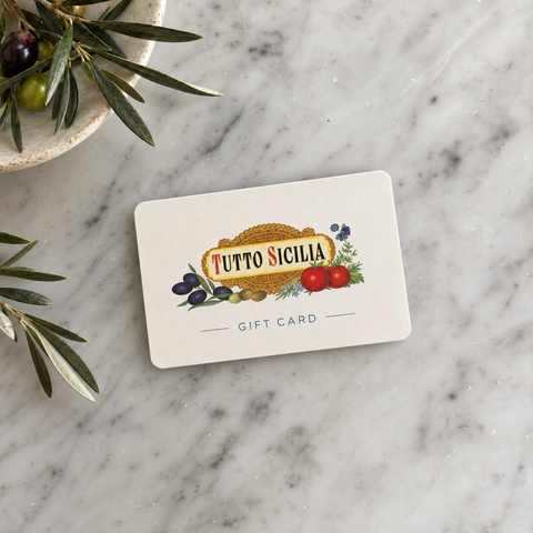 Tutto Sicilia Gift Card sitting on a marble counter top with olive branches in a bowl nearby.