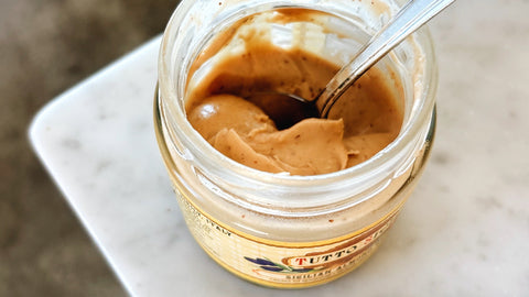 Jar of Sicilian Almond Cream on a marble counter top, opened with a spoon.