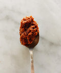 Spoonful of Sicilian sun-dried tomato paté on a marble surface.