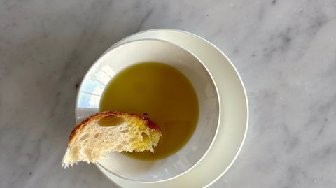Sicilian extra virgin olive oil in a white bowl with a piece of toasted bread, on white marble