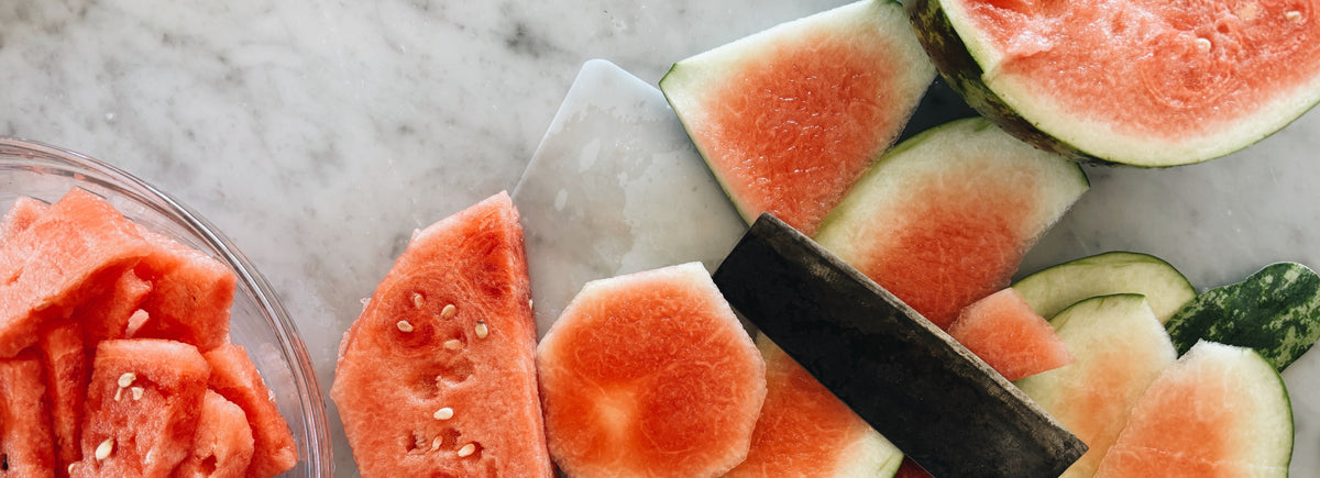 Cutting a fresh watermelon with a knife on a clear cutting mat to make gelo di melone, Sicilian watermelon pudding